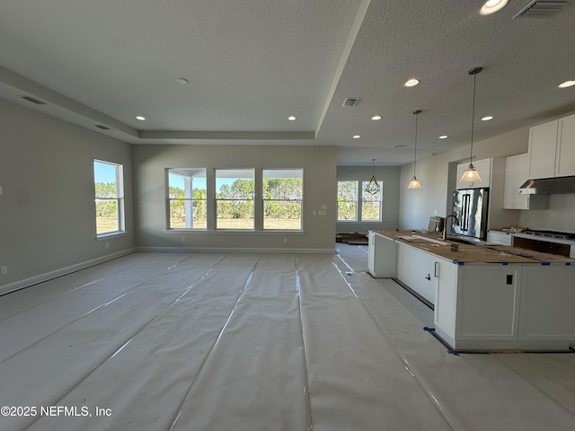 kitchen with open floor plan, stainless steel fridge, white cabinetry, and decorative light fixtures