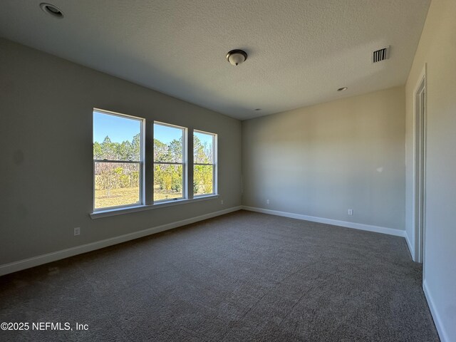 empty room with baseboards, visible vents, dark carpet, and a textured ceiling