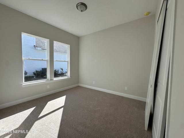 unfurnished room with dark carpet and baseboards