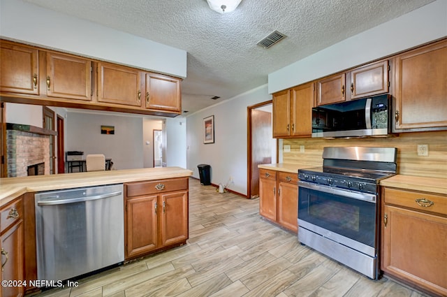 kitchen with light wood-type flooring, stainless steel appliances, a textured ceiling, and kitchen peninsula