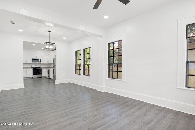 unfurnished living room with a healthy amount of sunlight, dark hardwood / wood-style floors, and ceiling fan with notable chandelier