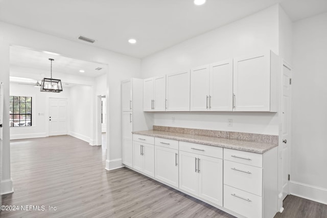 kitchen featuring light stone counters, hanging light fixtures, light wood-type flooring, a notable chandelier, and white cabinets