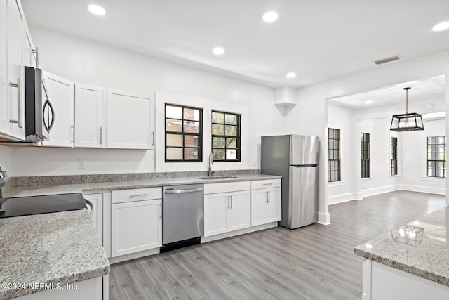 kitchen with white cabinetry, sink, hanging light fixtures, light stone counters, and stainless steel appliances