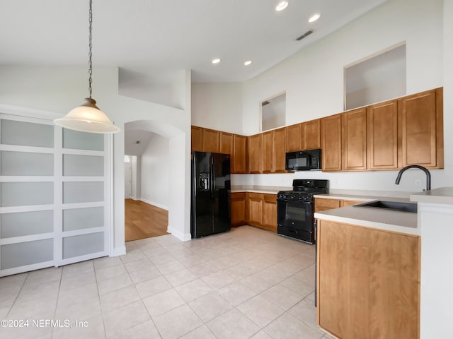 kitchen with hanging light fixtures, high vaulted ceiling, sink, black appliances, and light hardwood / wood-style flooring