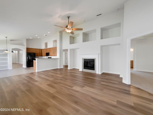 unfurnished living room featuring ceiling fan, light wood-type flooring, and a towering ceiling