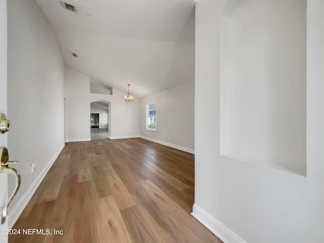 unfurnished living room featuring wood-type flooring, vaulted ceiling, and an inviting chandelier