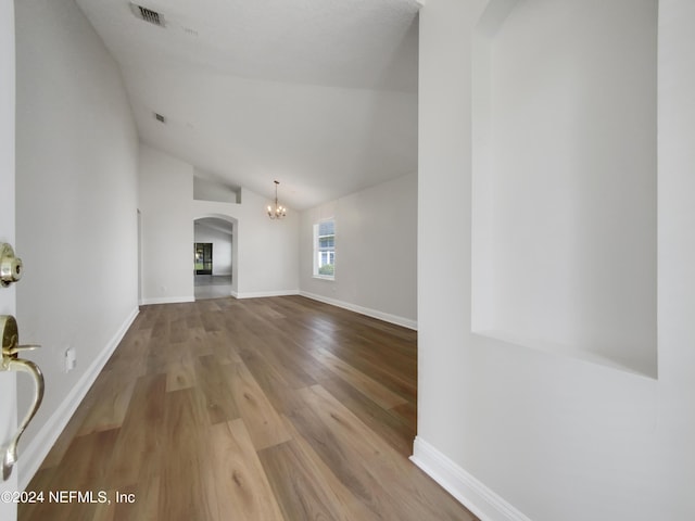 unfurnished living room featuring light hardwood / wood-style floors, a chandelier, and lofted ceiling