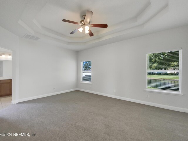 unfurnished room with ceiling fan, a raised ceiling, and light colored carpet