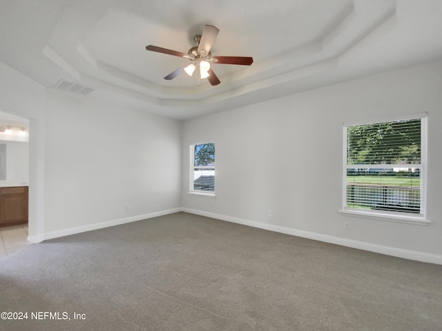 carpeted spare room with a raised ceiling and ceiling fan