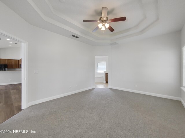 carpeted spare room with ceiling fan and a tray ceiling