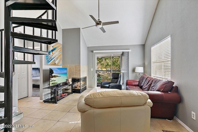 living area featuring light tile patterned floors, ceiling fan, high vaulted ceiling, a tile fireplace, and baseboards