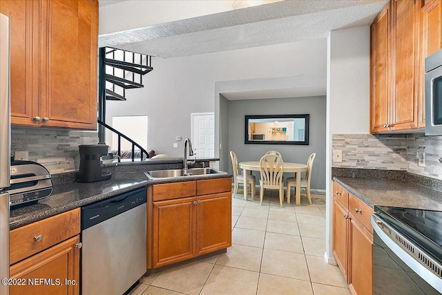 kitchen featuring appliances with stainless steel finishes, dark stone countertops, sink, light tile patterned floors, and decorative backsplash