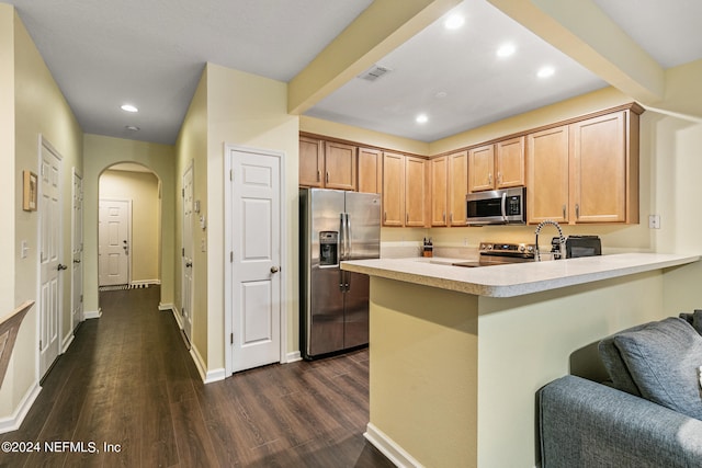 kitchen with appliances with stainless steel finishes, beam ceiling, dark wood-type flooring, light brown cabinetry, and kitchen peninsula