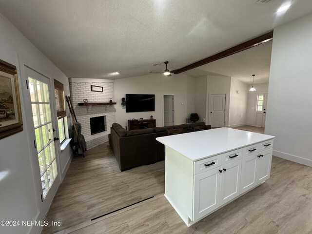 kitchen with vaulted ceiling with beams, light countertops, light wood-type flooring, a fireplace, and white cabinetry