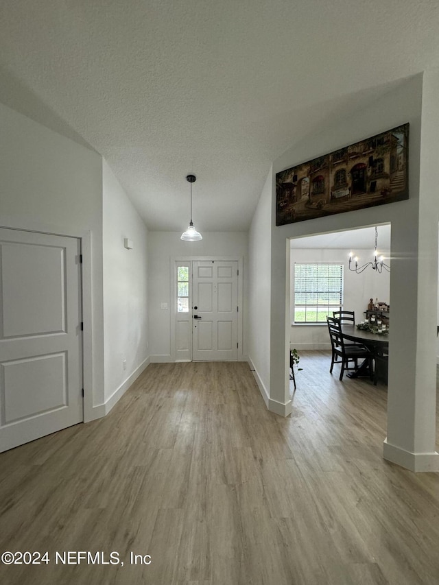 entryway featuring light wood-style floors, baseboards, a textured ceiling, and an inviting chandelier