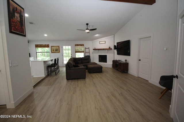 living room featuring a brick fireplace, visible vents, light wood finished floors, and beamed ceiling