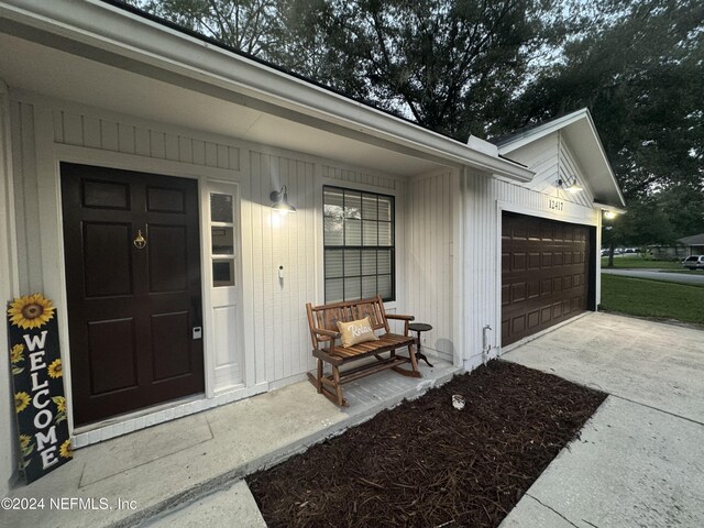 doorway to property with a porch, concrete driveway, and an attached garage