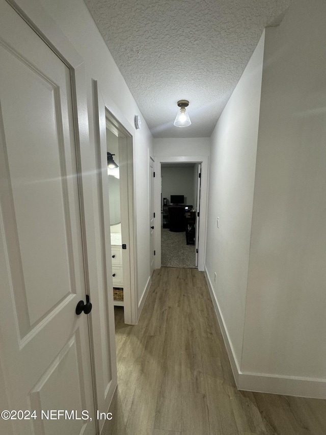 hall featuring a textured ceiling, baseboards, and wood finished floors