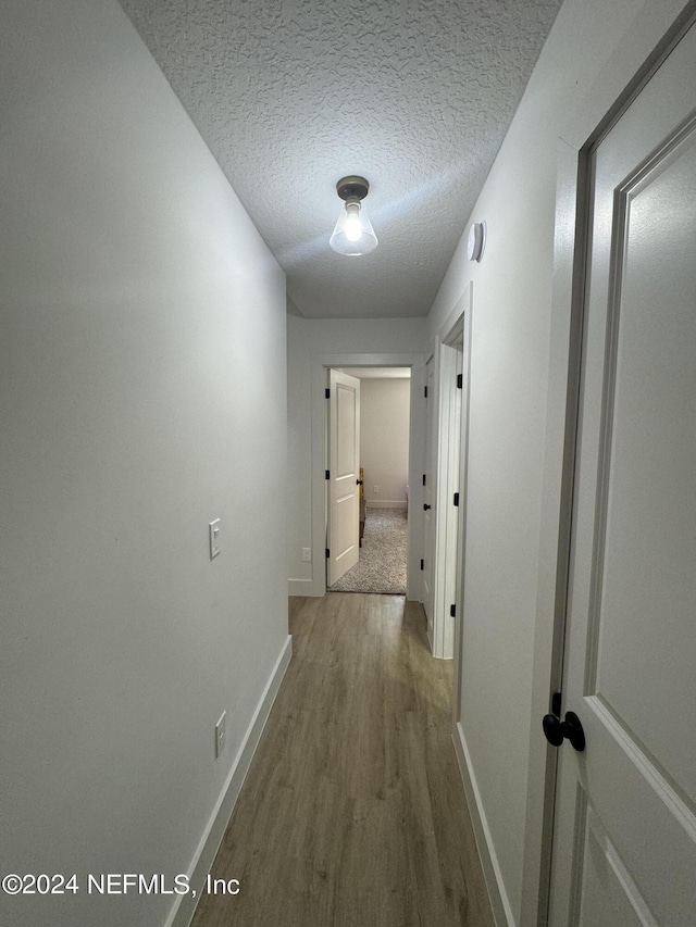 corridor with a textured ceiling, wood finished floors, and baseboards