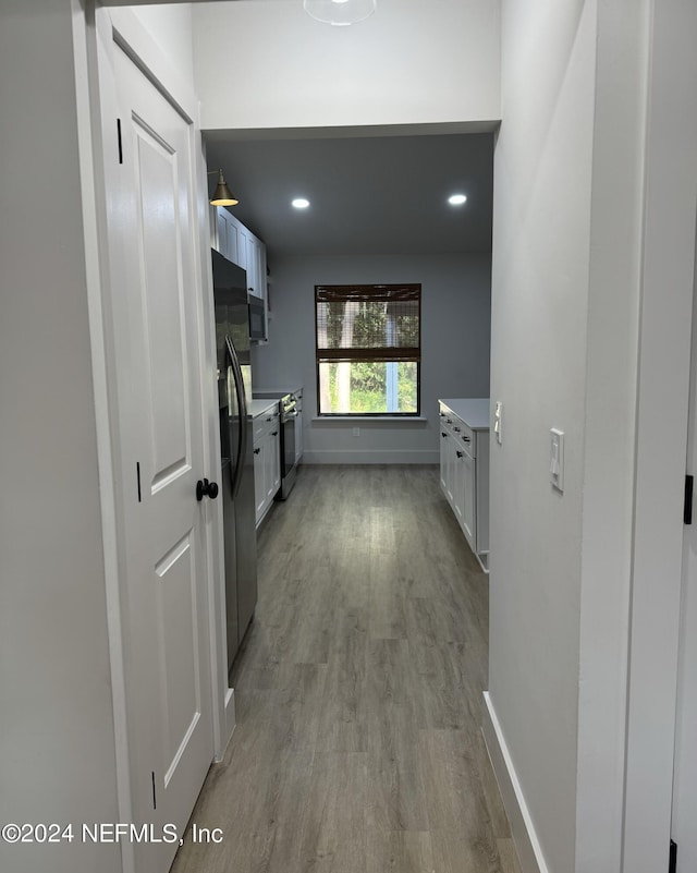 hallway featuring light wood finished floors, baseboards, and recessed lighting