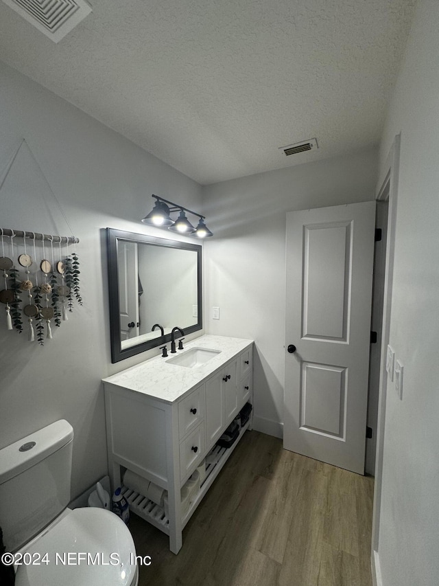 bathroom with toilet, vanity, wood finished floors, and visible vents