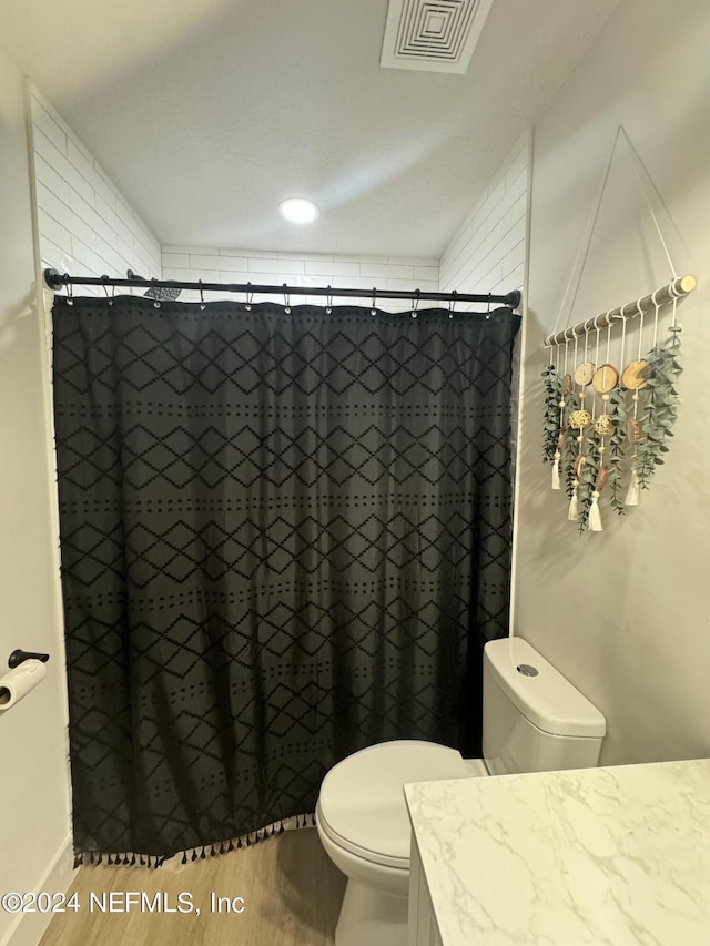 full bath with visible vents, a shower with shower curtain, toilet, wood finished floors, and vanity