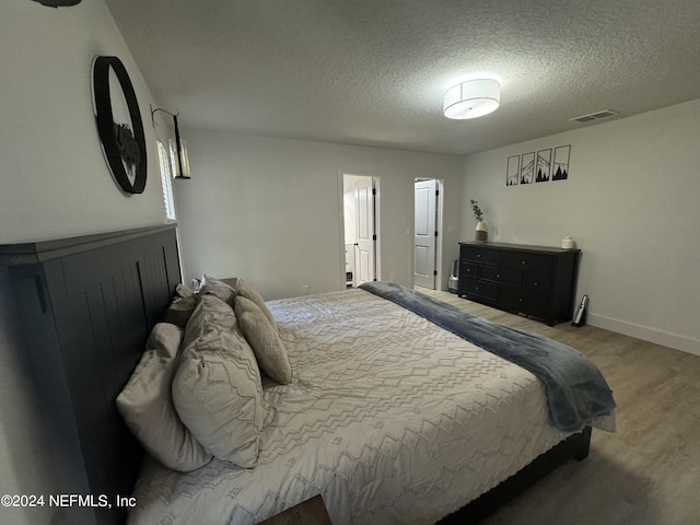 bedroom featuring baseboards, a textured ceiling, visible vents, and wood finished floors