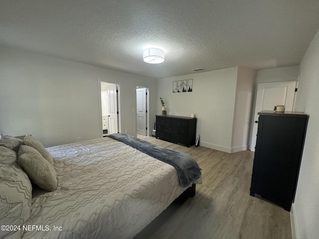 bedroom with visible vents, baseboards, light wood-style flooring, and a textured ceiling