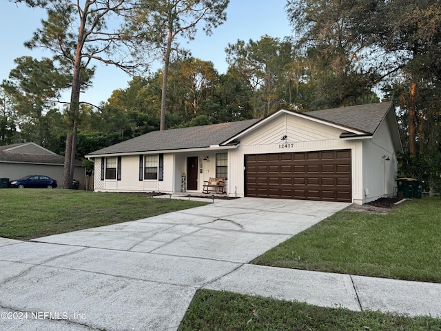 ranch-style house with concrete driveway, a front lawn, roof with shingles, and an attached garage