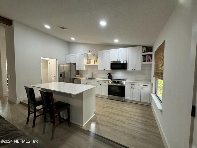 kitchen featuring open shelves, stainless steel appliances, lofted ceiling, white cabinetry, and a sink