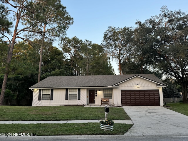 ranch-style home with a garage, driveway, a front lawn, and roof with shingles