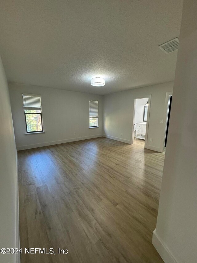 unfurnished room featuring a wealth of natural light, visible vents, a textured ceiling, and wood finished floors