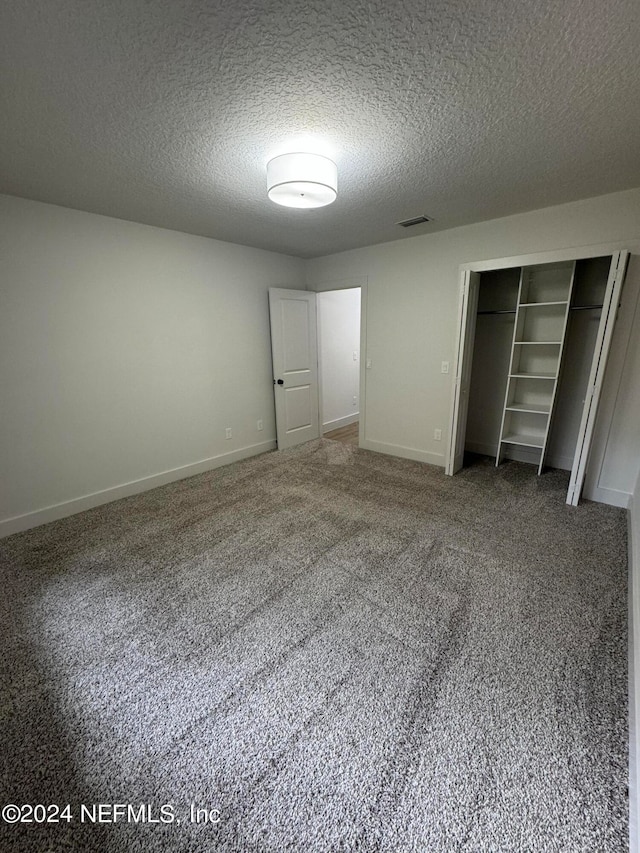 unfurnished bedroom with baseboards, visible vents, a textured ceiling, carpet flooring, and a closet