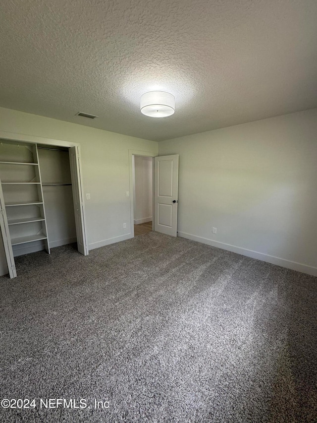 unfurnished bedroom featuring baseboards, visible vents, carpet, a textured ceiling, and a closet