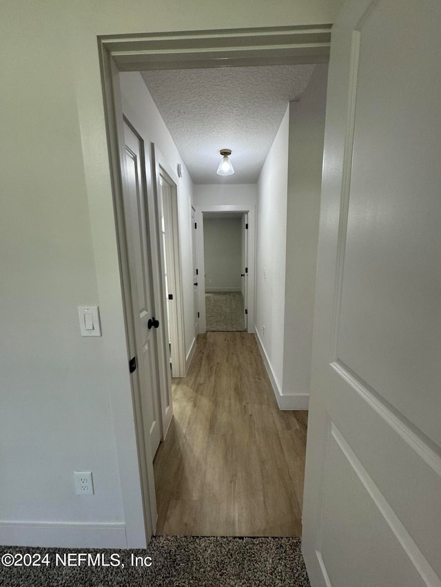 hallway featuring a textured ceiling, baseboards, and wood finished floors