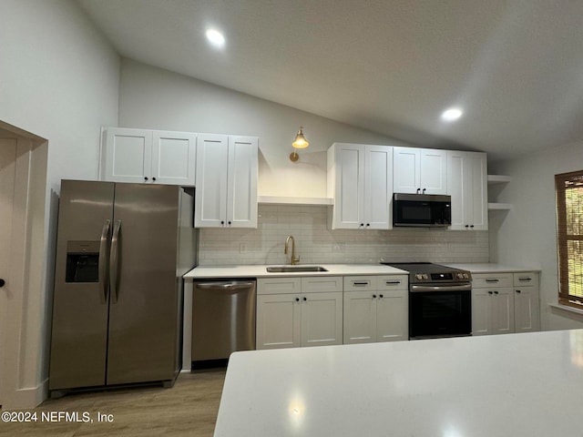 kitchen featuring lofted ceiling, appliances with stainless steel finishes, light countertops, open shelves, and a sink