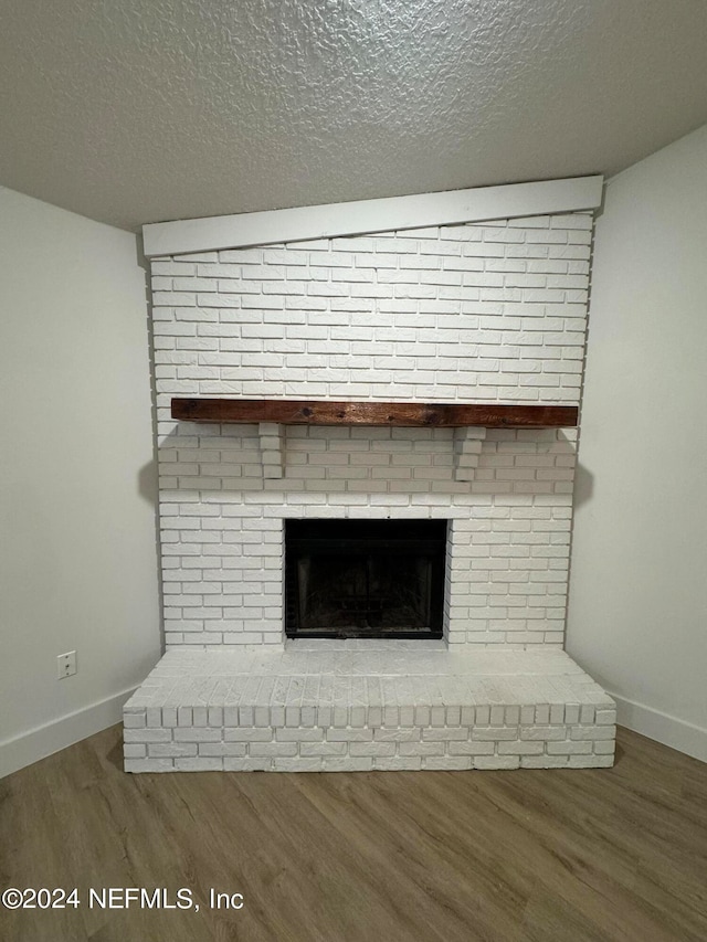 details with a textured ceiling, a brick fireplace, wood finished floors, and baseboards