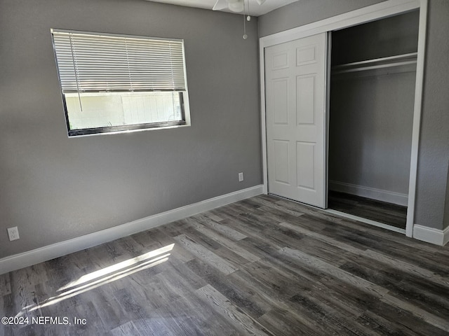 unfurnished bedroom with dark wood-type flooring, a closet, and baseboards