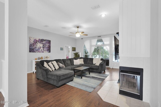 living room featuring a tiled fireplace, ceiling fan, and wood-type flooring