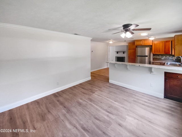 kitchen with a peninsula, a kitchen breakfast bar, light countertops, freestanding refrigerator, and brown cabinetry