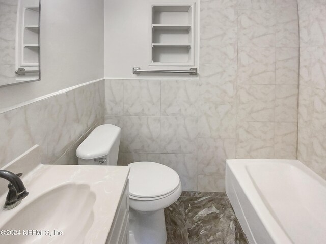 bathroom featuring toilet, vanity, tile walls, marble finish floor, and a bath