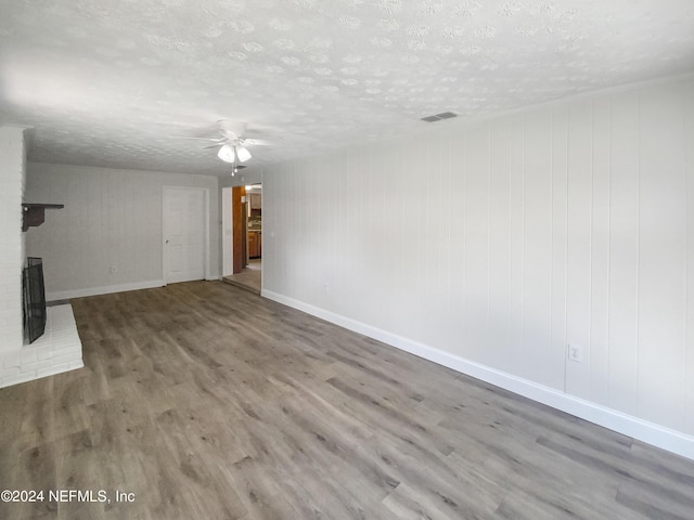 unfurnished living room featuring visible vents, ceiling fan, wood finished floors, a textured ceiling, and a brick fireplace