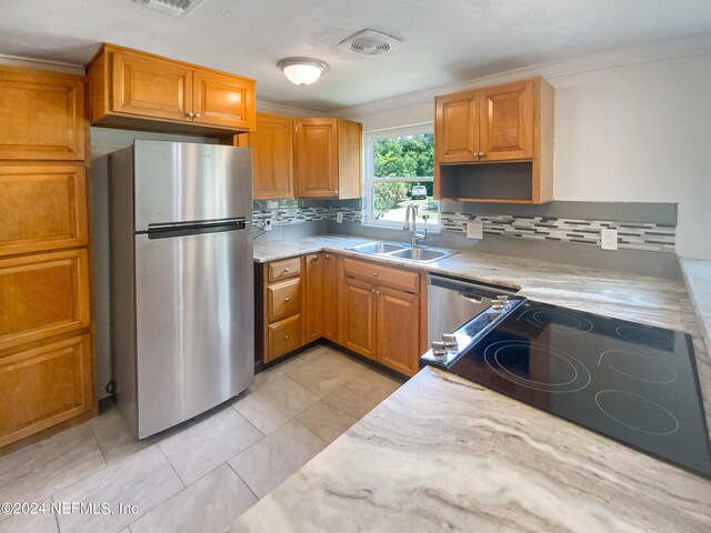 kitchen featuring light tile patterned floors, stainless steel appliances, a sink, decorative backsplash, and brown cabinetry