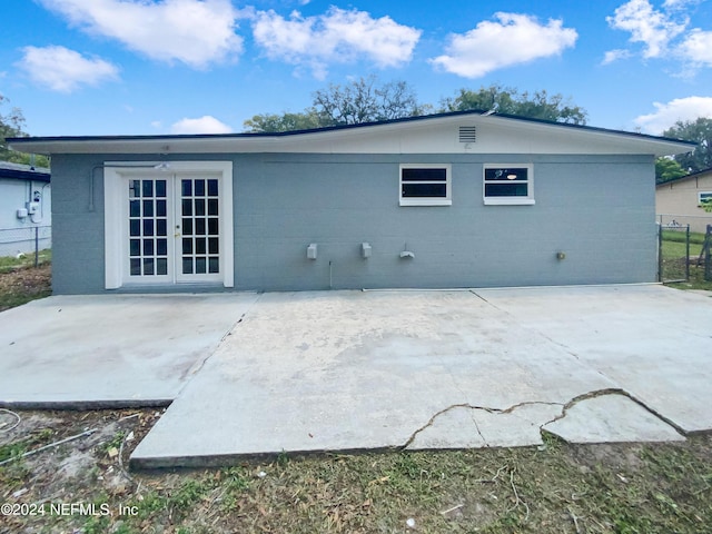 rear view of house with french doors, a patio area, concrete block siding, and fence