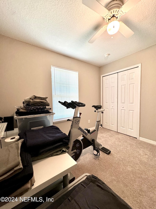 exercise area featuring a textured ceiling, ceiling fan, and carpet floors