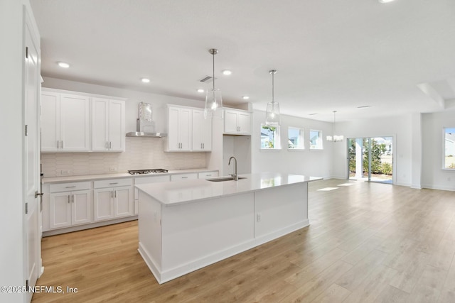 kitchen with wall chimney exhaust hood, sink, an island with sink, stainless steel gas stovetop, and white cabinets