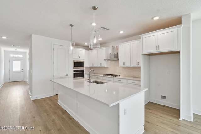 kitchen with pendant lighting, sink, appliances with stainless steel finishes, a kitchen island with sink, and white cabinets