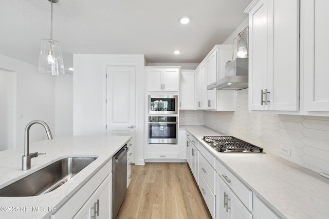 kitchen with sink, white cabinetry, appliances with stainless steel finishes, pendant lighting, and wall chimney range hood