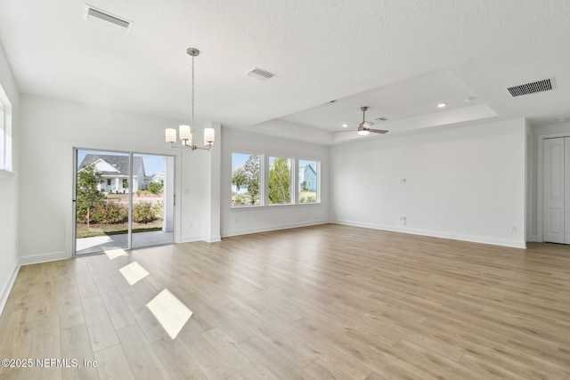 unfurnished living room featuring a tray ceiling, ceiling fan with notable chandelier, a textured ceiling, and light wood-type flooring