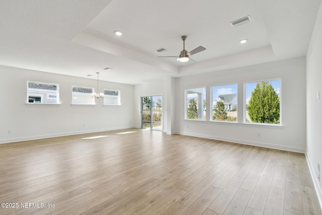 unfurnished room with a tray ceiling, ceiling fan with notable chandelier, and light wood-type flooring